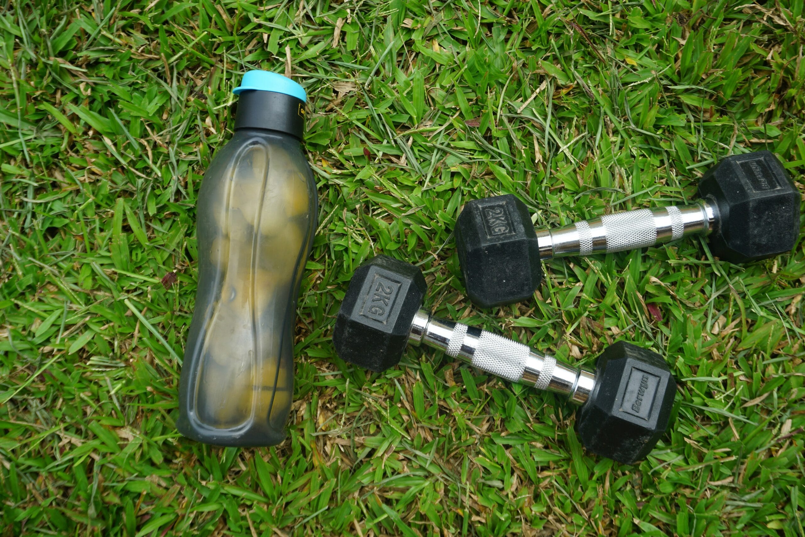 Water bottle and dumbbells on grass symbolizing outdoor fitness training
