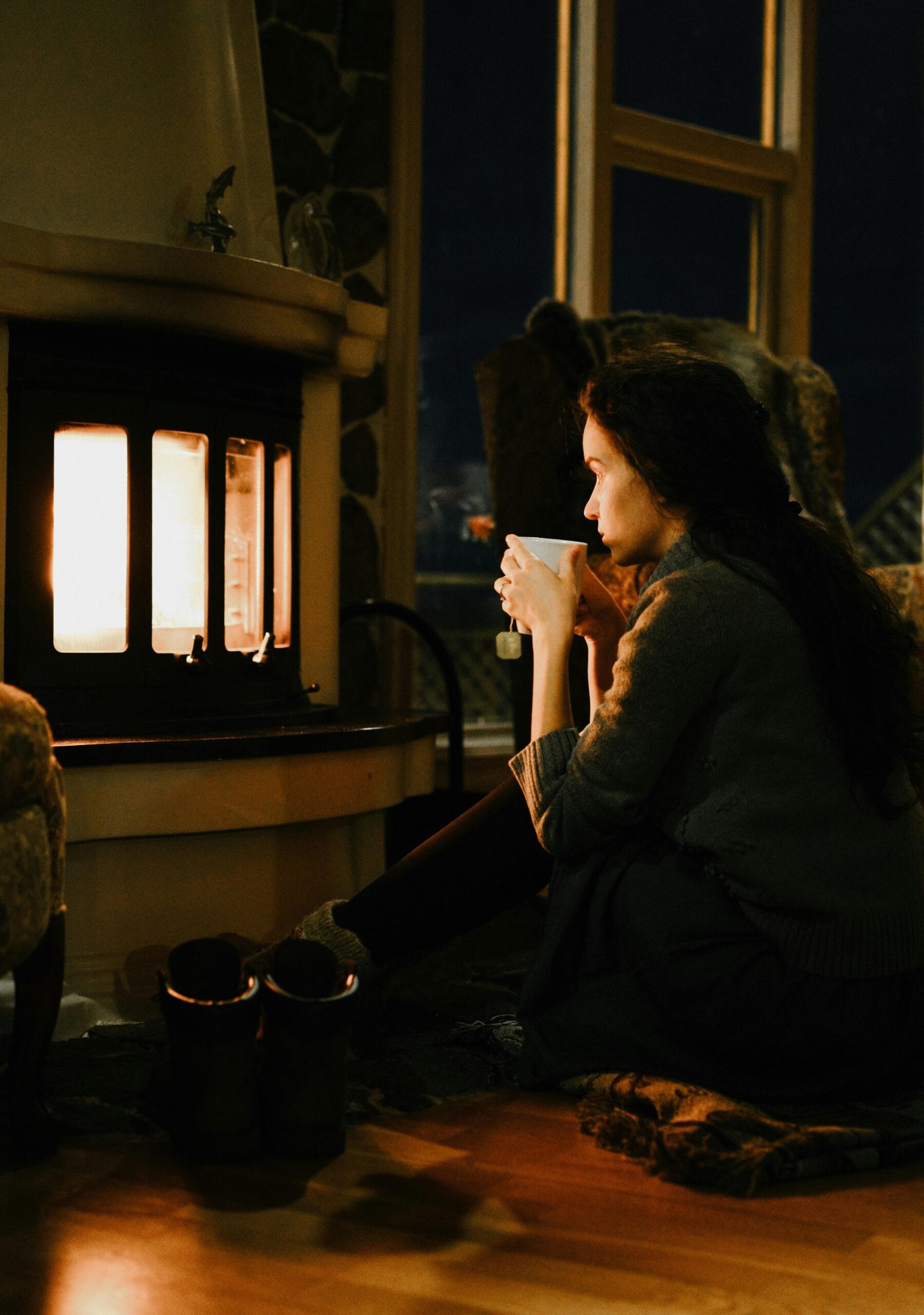 Woman drinking tea at home by the fireplace, focusing on recovery and warmth during winter.