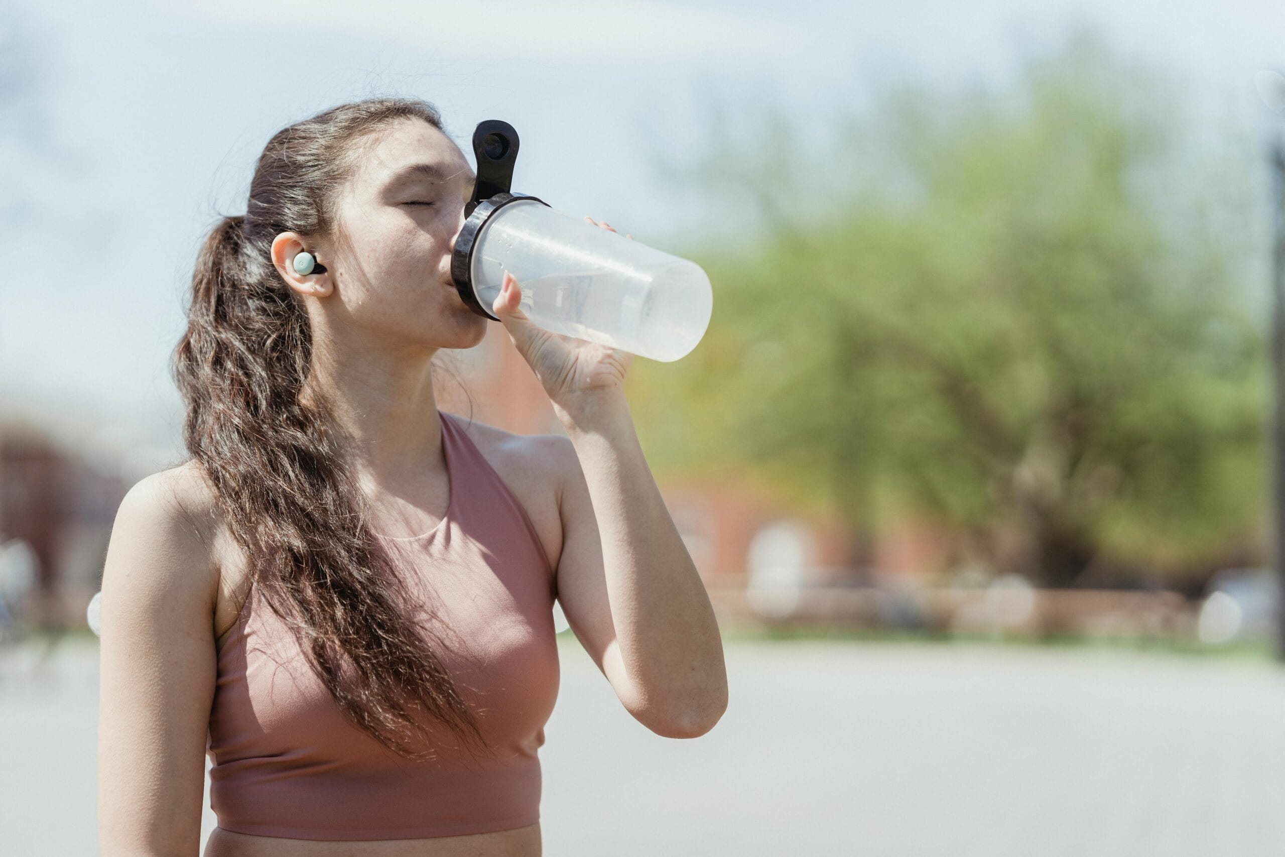 A woman drinking water in a park.
